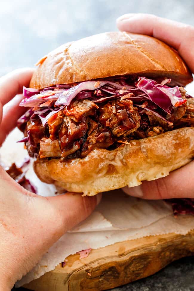 holding a bbq beef brisket sandwich with two hands on a cutting board