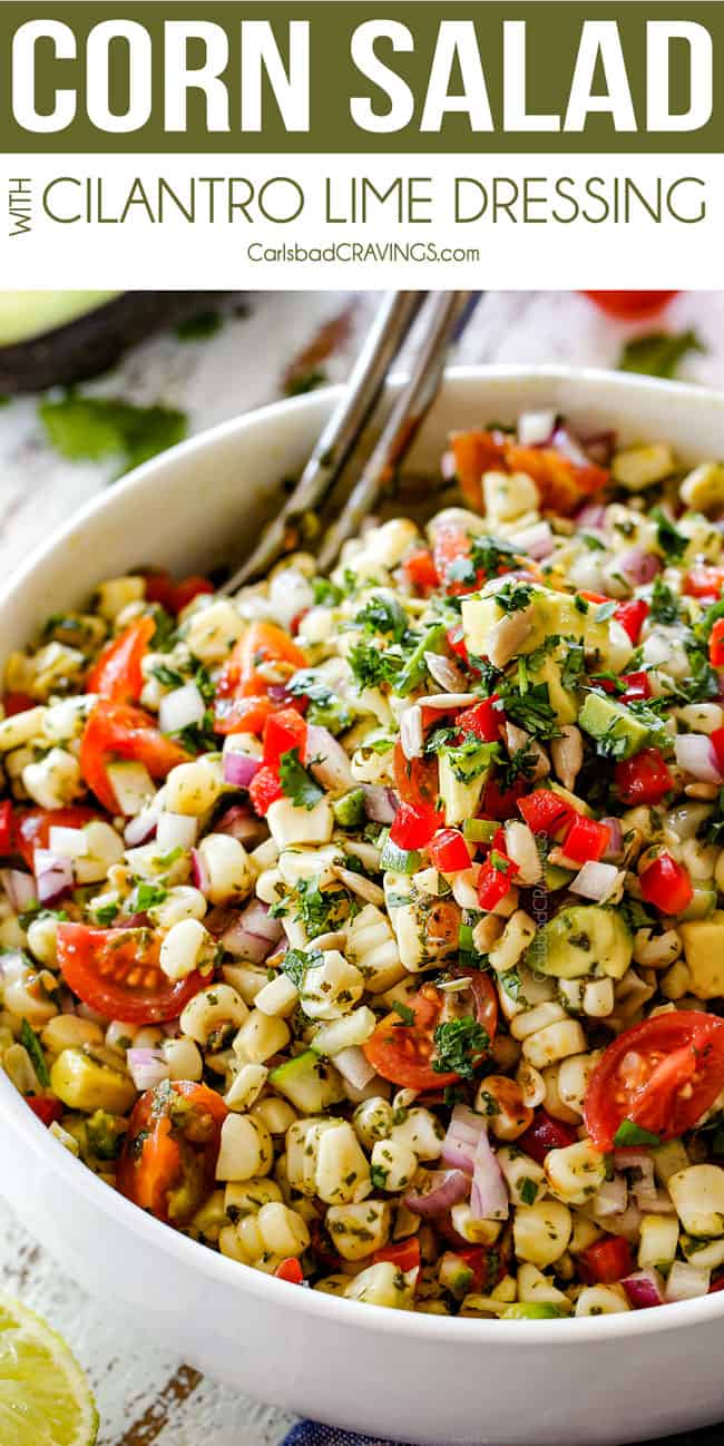 Fresh Corn Salad with avocado, red bell peppers, jalapeno, cilantro, sesame seeds mixed together in a white bowl with silver spoons