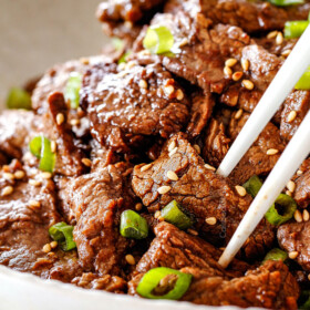 using chopsticks to pick up Beef Bulgogi in a white dish with sesame seeds and green onions
