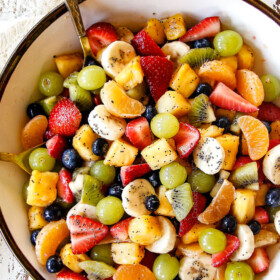 top view of best fruit salad in bowl with pineapple, strawberries, blueberries, bananas, kiwis, grapes and oranges