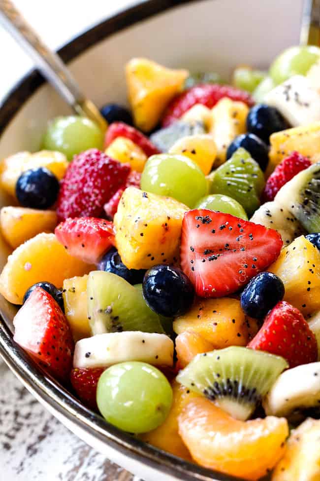 healthy fruit salad in bowl with pineapple, strawberries, blueberries, bananas, kiwis, grapes and oranges