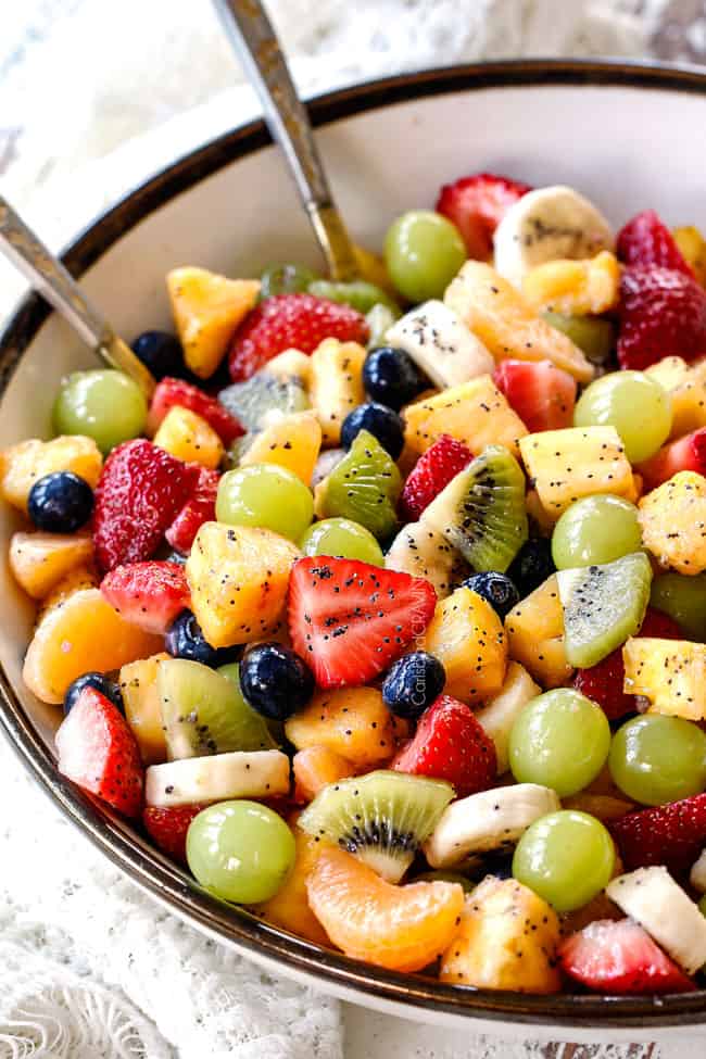 healthy fruit salad in bowl with pineapple, strawberries, blueberries, bananas, kiwis, grapes and oranges