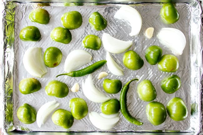 showing how to make authentic salsa verde with a top view of tomatillos, serranos, onions and garlic on a baking sheet 
