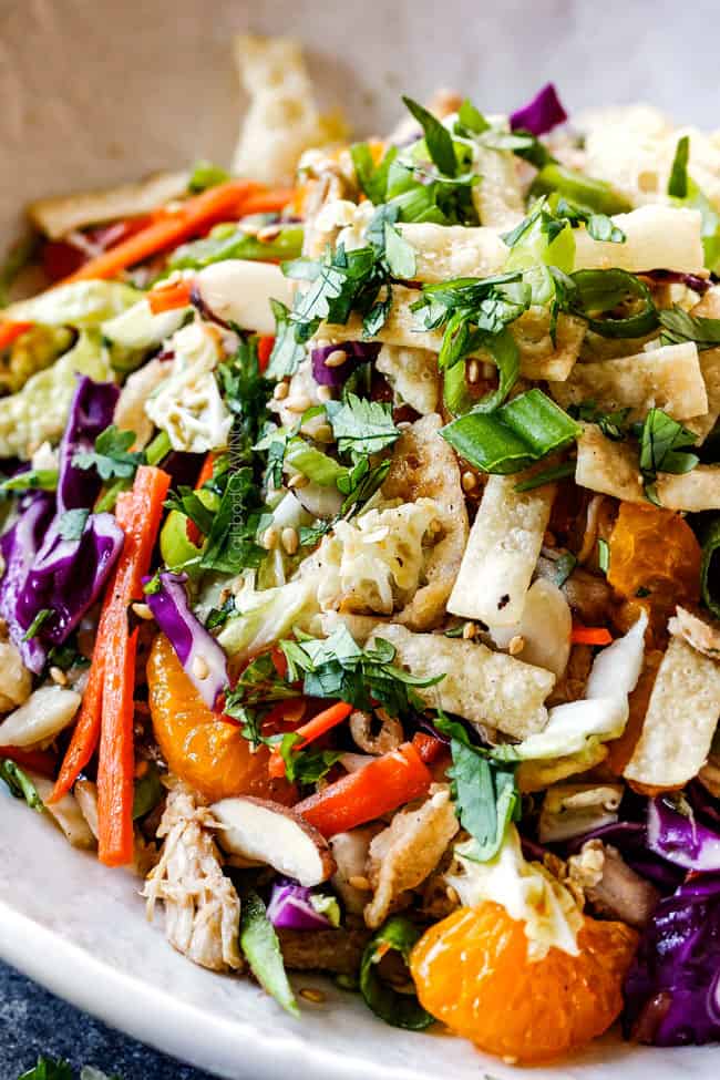 up close side view of top view of crunchy Chinese chicken salad with ramen noodles, Mandarin oranges, peanuts napa cabbage, wontons, carrots, snow peas, red bell peppers all tossed together with sesame dressing