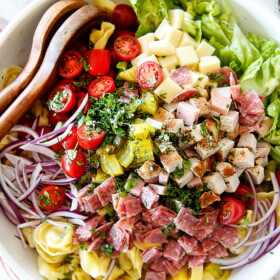 top view of Cuban pasta salad with cheesy tortellini, cubed pork roast, ham, salami, Swiss cheese, tomatoes, pickles pickled jalapenos, red onions, Romaine lettuce and cilantro