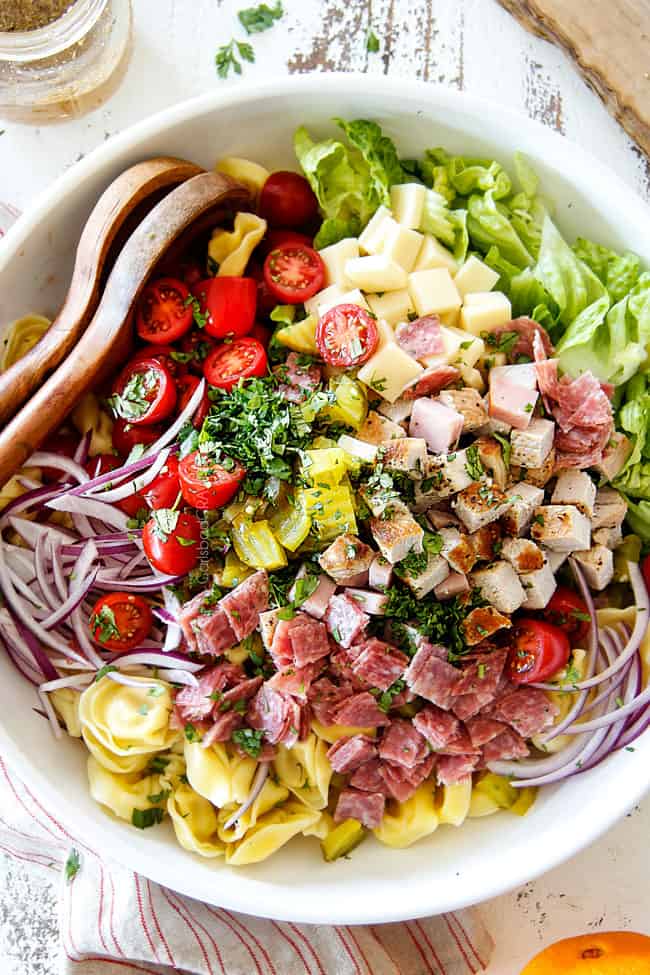 top view of Cuban pasta salad with cheesy tortellini, cubed pork roast, ham, salami, Swiss cheese, tomatoes, pickles pickled jalapenos, red onions, Romaine lettuce and cilantro