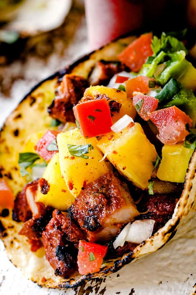 up close of Tacos Al Pastor with chopped al pastor, pineapple, pico de gallo and guacamole