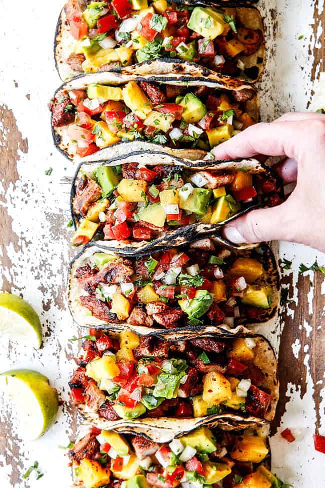 top view of a line of tacos al pastor with a hand grabbing one of the tacos