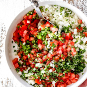 showing how to make authentic pico de gallo by stirring together tomatoes, cilantro, onions, jalapenos, lime juice in a white bowl