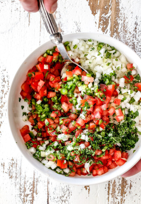 showing how to make authentic pico de gallo by stirring together tomatoes, cilantro, onions, jalapenos, lime juice in a white bowl