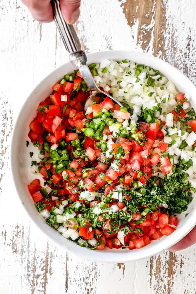 Showing how to make pico de gallo by stirring tomatoes, onions, cilantro, jalapenos together in a white bowl