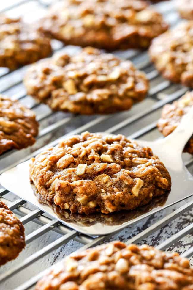 showing how to make oatmeal apple cookies with a spatula picking up an apple cookie on a cooling rack