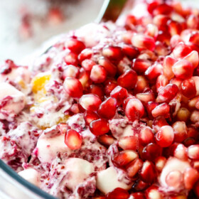up close of a spoon scooping classic ambrosia salad with pineapple, mandarin oranges, mini marshmallows, cranberries and pomegranate seeds in a glass bowl