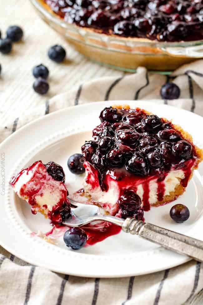 a slice of easy blueberry cheesecake on a plate with a fork taking a bite