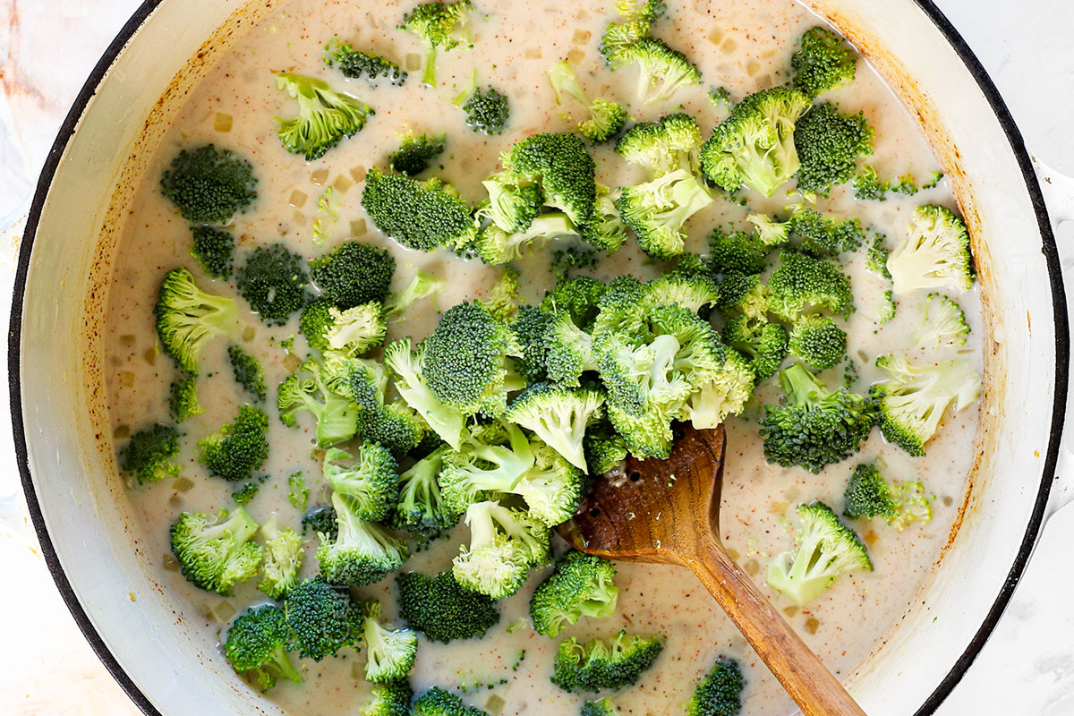 showing how to make broccoli cheese soup by adding the chicken broth, milk, spices and broccoli