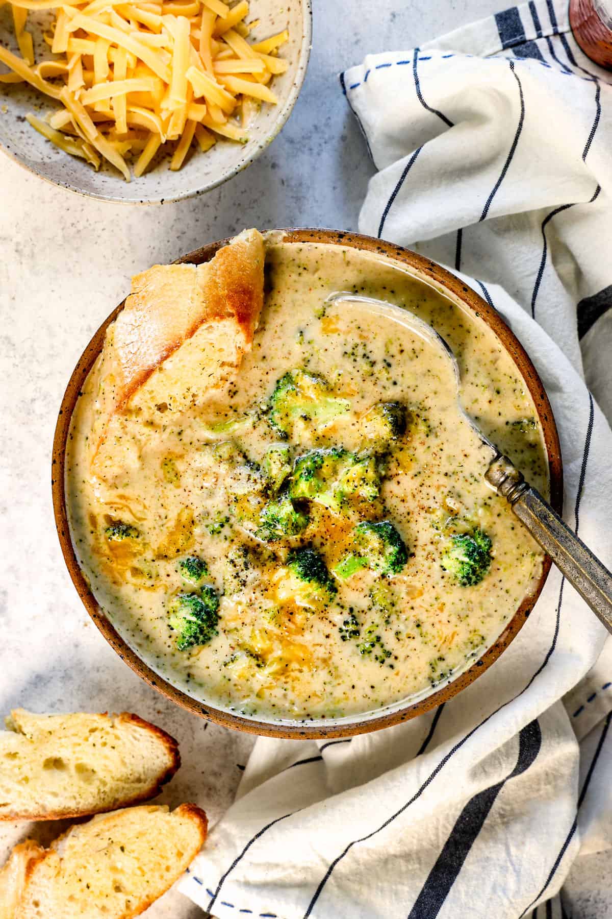 showing how to serve broccoli cheese soup garnished with extra cheese and baguette slices for dipping