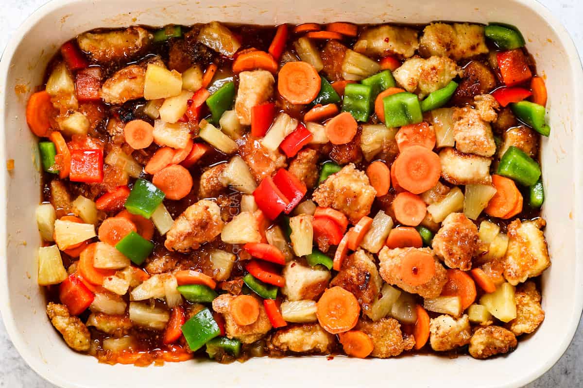 showing how to make sweet and sour chicken by stirring the chicken, sweet and sour sauce, carrots, pineapple and bell peppers together in a 9x13 baking dish