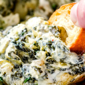 up close of a piece of bread dipping into spinach and artichoke dip