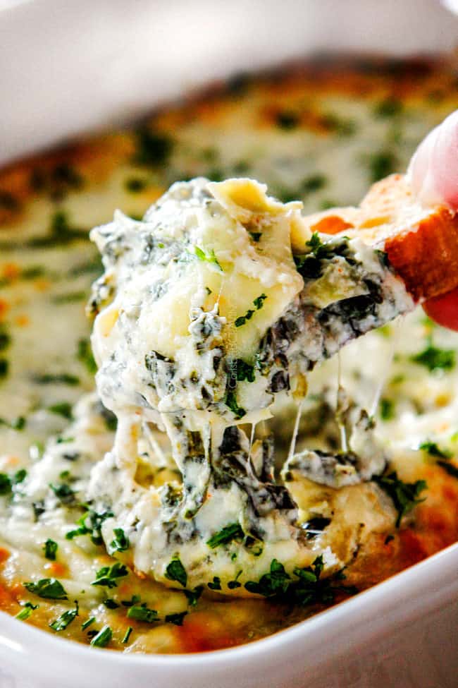 up close of bread being pulled from hot spinach artichoke dip with cheese 