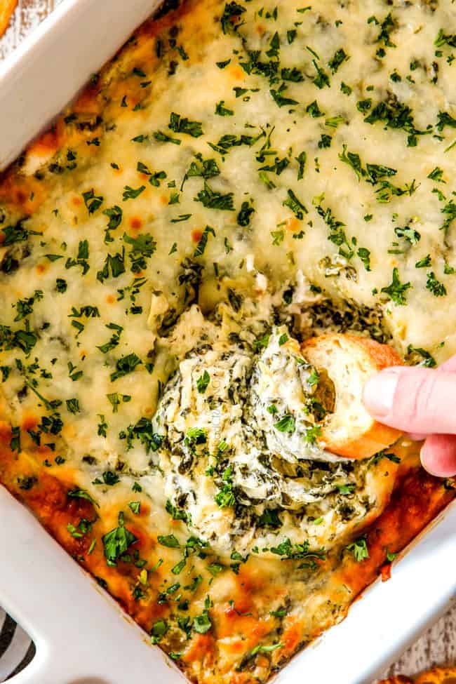 up close top view of a piece of bread dipping into cheesy spinach artichoke dip