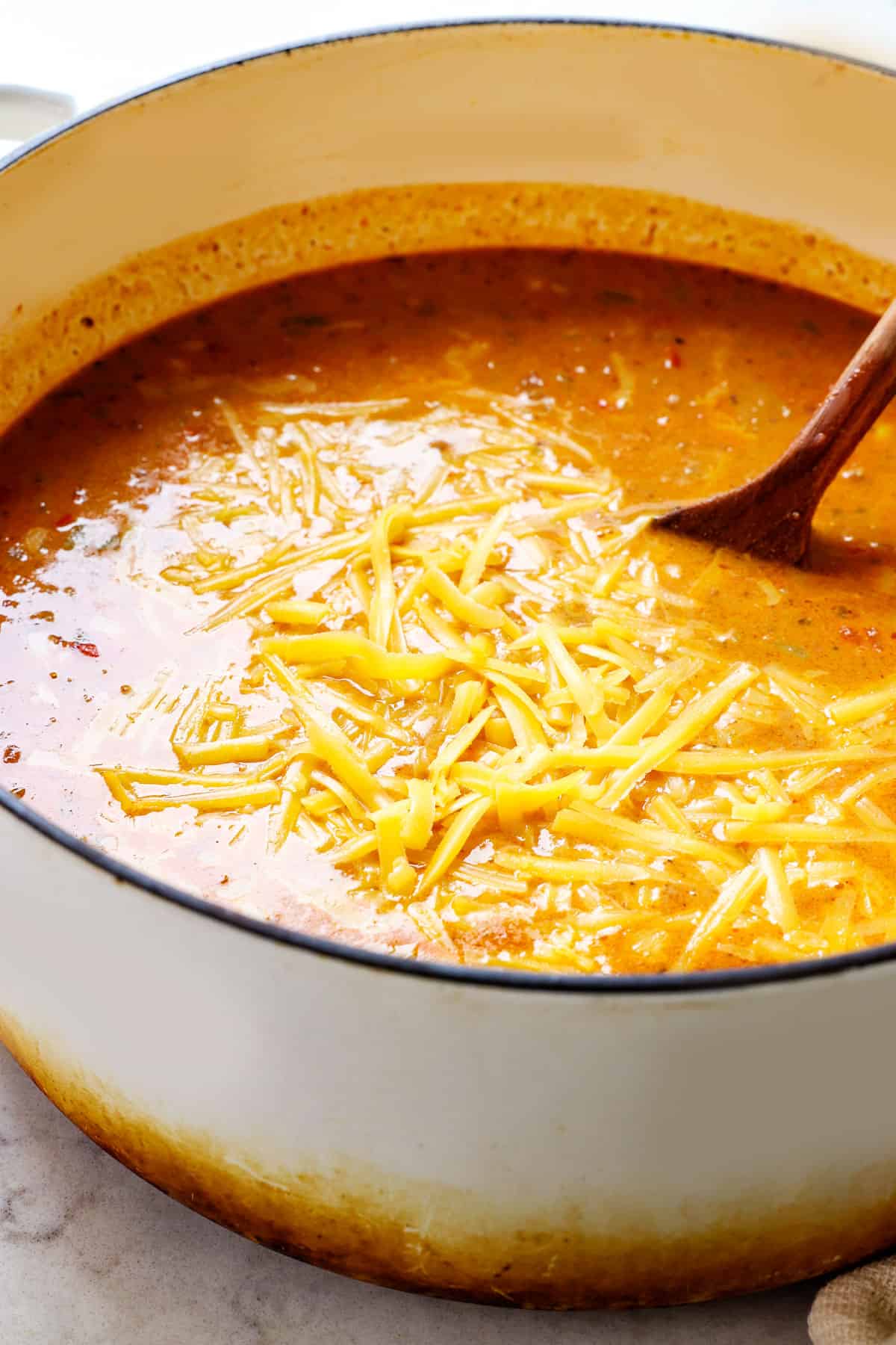 showing how to make taco soup by stirring cheese into the soup pot