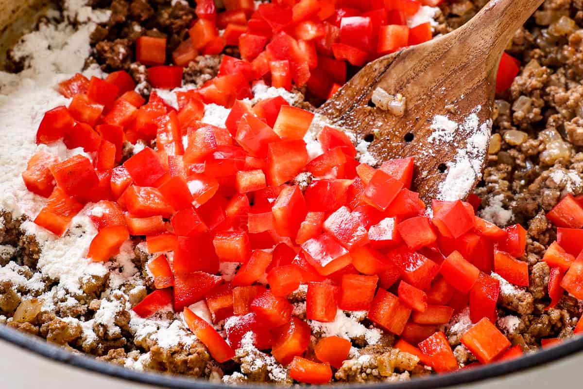 showing how to make taco soup recipe by adding red bell pepper, garlic and flour to the ground beef