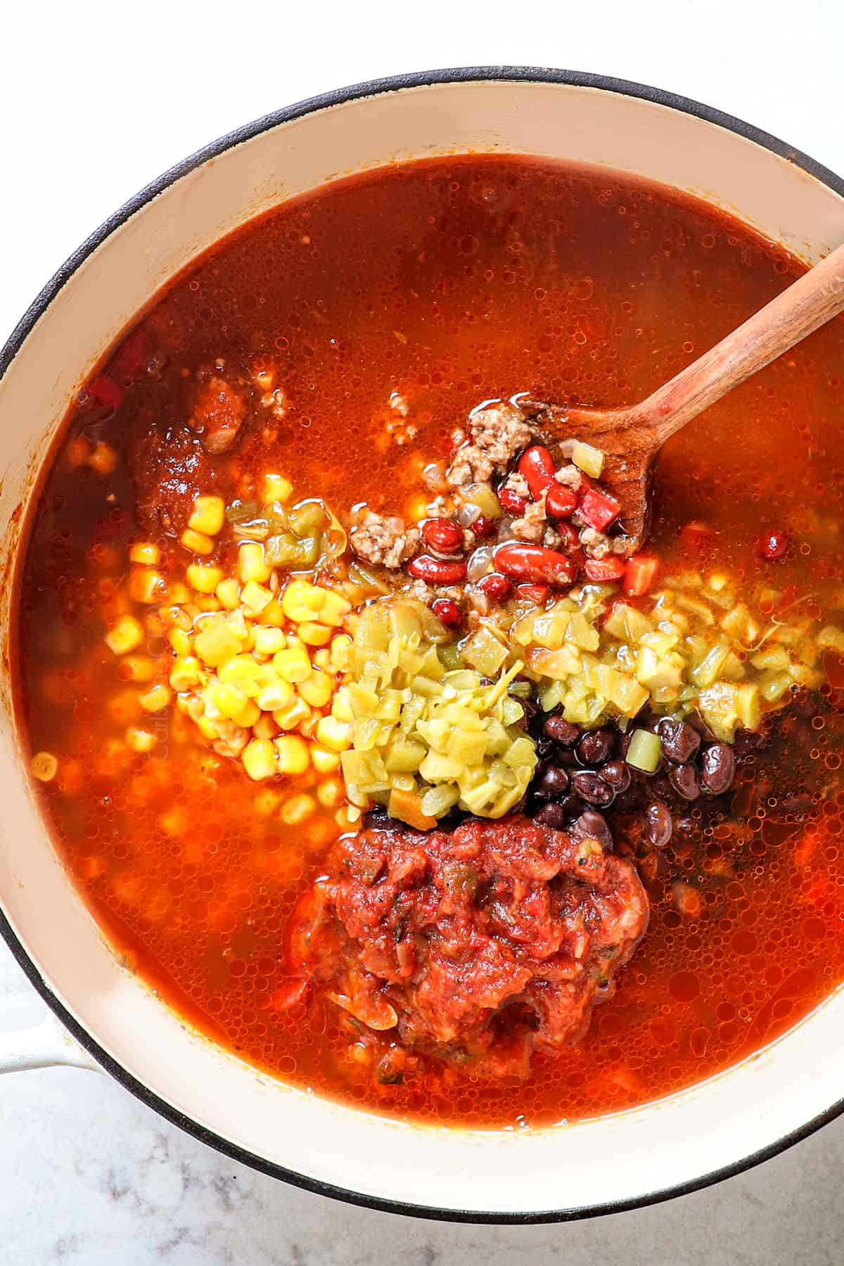 showing how to make taco soup recipe by stirring in black beans, kidney beans, corn, enchilada sauce, salsa and chicken broth into the soup pot