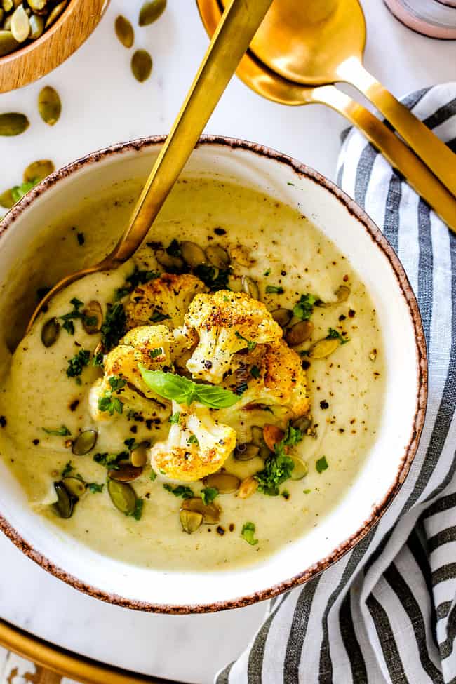 top view of creamy cauliflower soup garnished with roasted cauliflower, parsley and pepitas