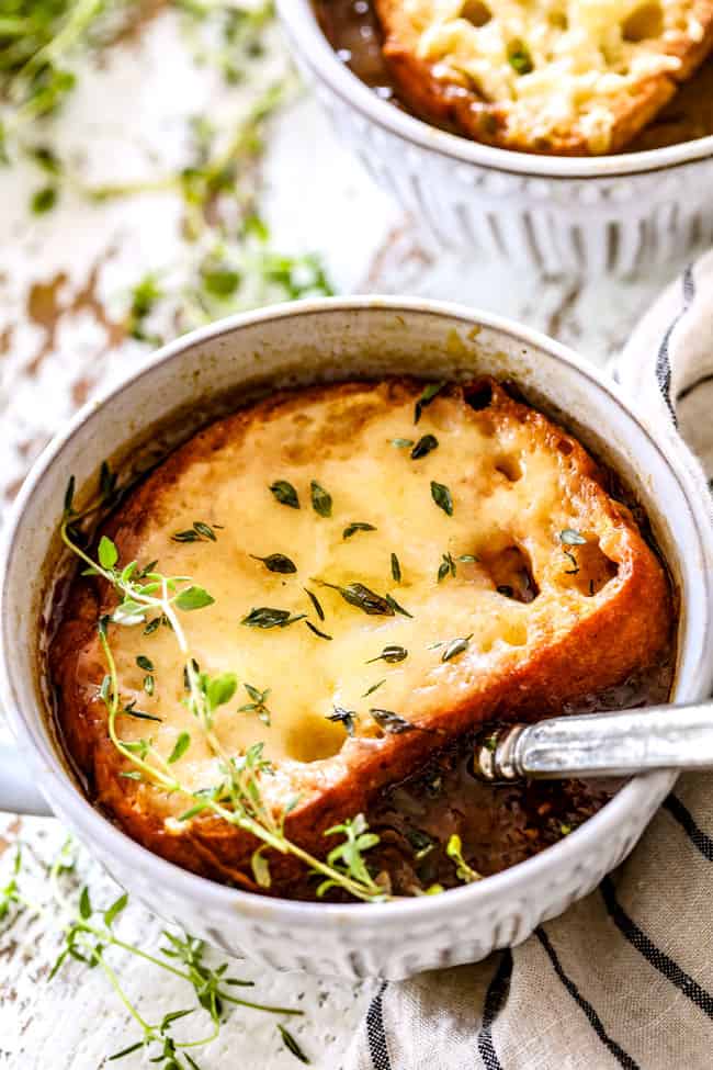 side view of a bowl of traditional French Onion Soup with a spoon a fresh thyme