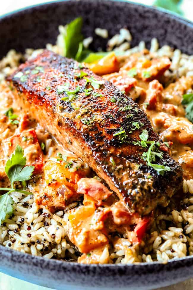 a piece of blackned salmon on a bed of rice with Cajun sauce and bell peppers