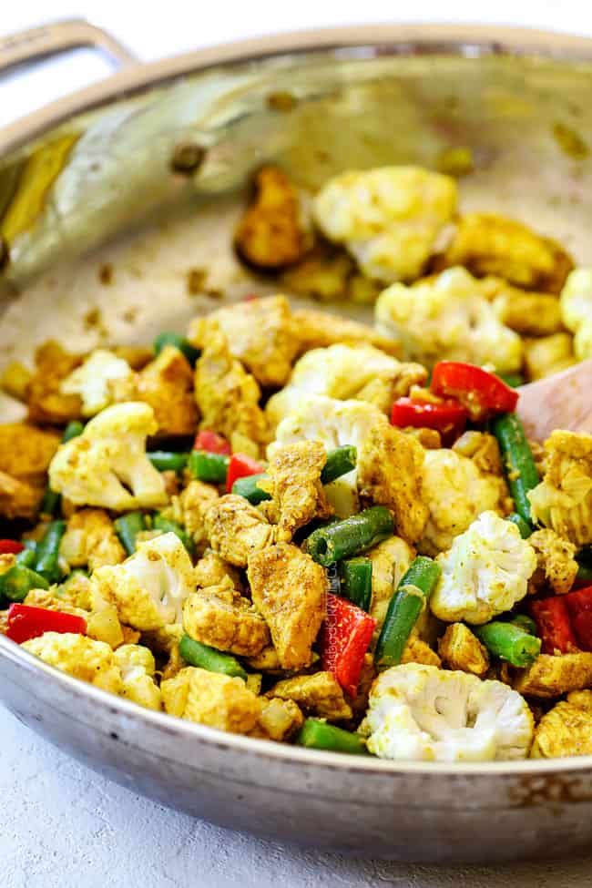 showing how to make coconut curry chicken recipe by cooking curry powder, chicken and vegetables in a skillet