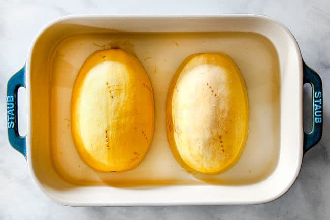 showing how to cook spaghetti squash in the microwave by placing two spaghetti squash halves cut side down in water in a pan