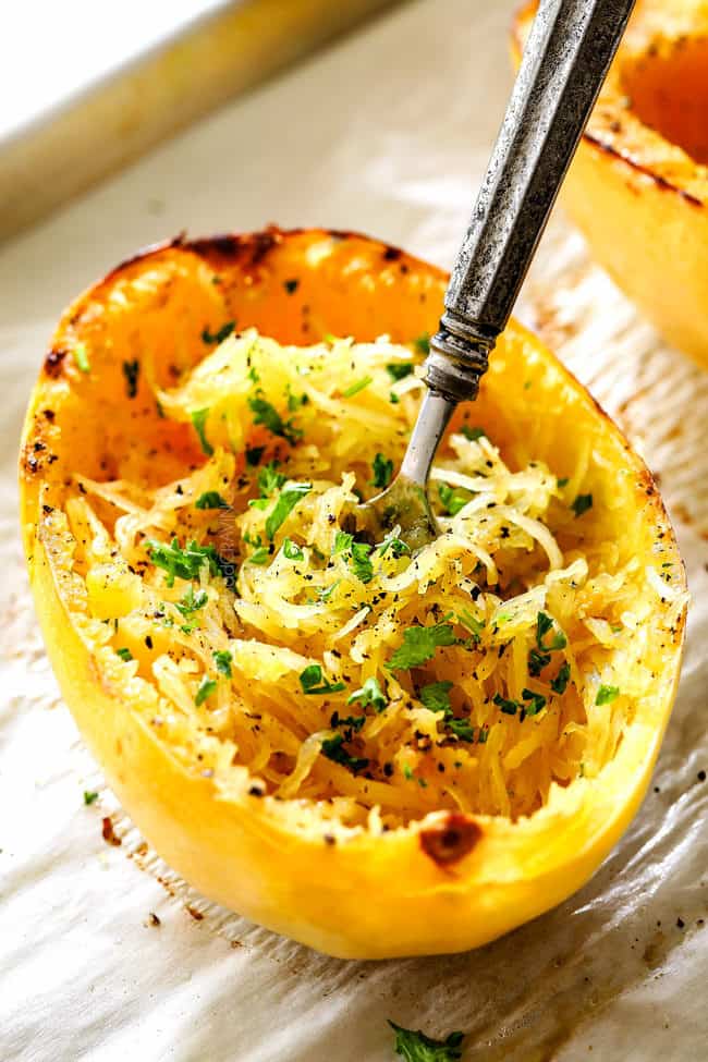 a roasted spaghetti squash half on a baking sheet garnished with Parmesan and parsley