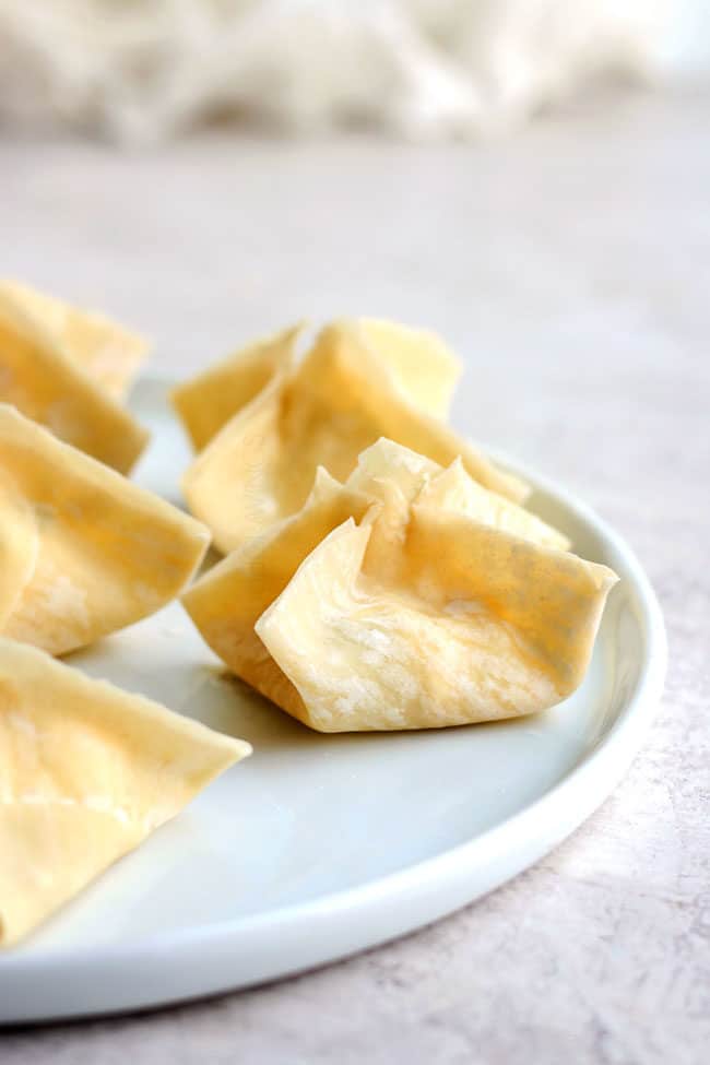 showing how to make cream cheese wontons by placing folded wontons on a plate