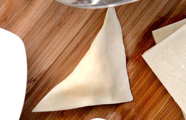 showing how tot fold wonton wrapper by folding over into a triangle