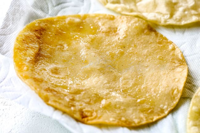 showing how to make chicken enchiladas by draining fried corn tortillas on a paper towel