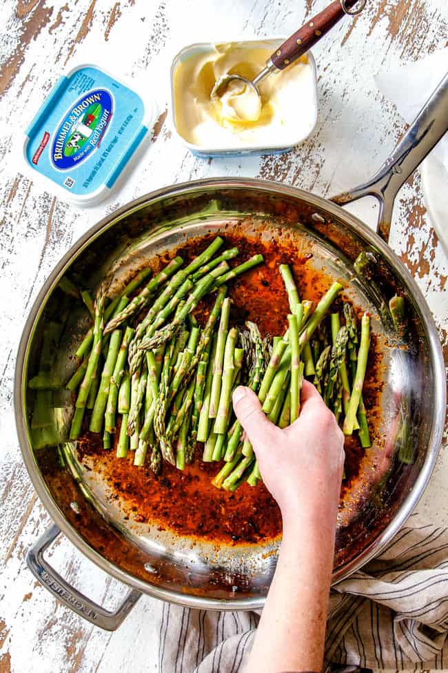 showing how to make lemon pepper chicken by adding asparagus to skillet