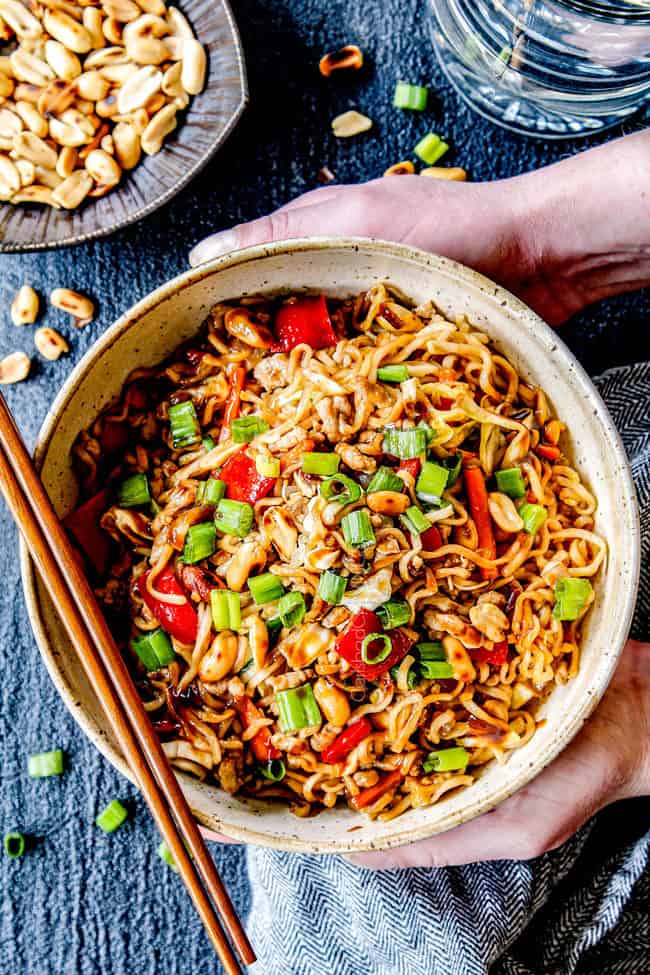 two hands holding a big bowl of spicy ramen with pork