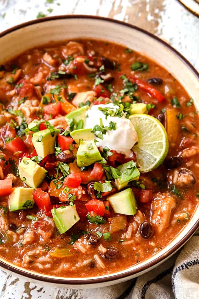 up close of a bowl of chicken fajita soup garnished with tomatoes, avocados, cilantro and sour cream