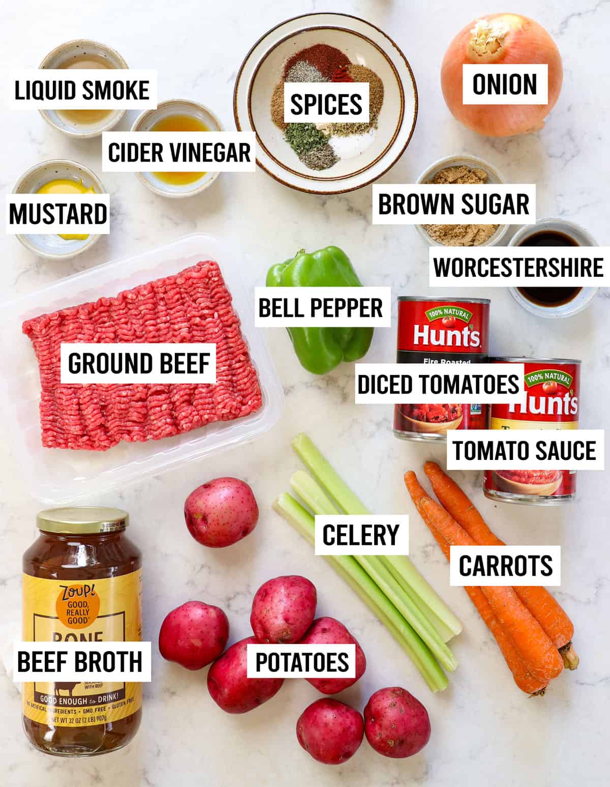 top view of hamburger soup ingredients: ground beef, potatoes, carrots, celery, bell pepper, beef broth, tomato sauce, diced tomatoes, onions and garlic