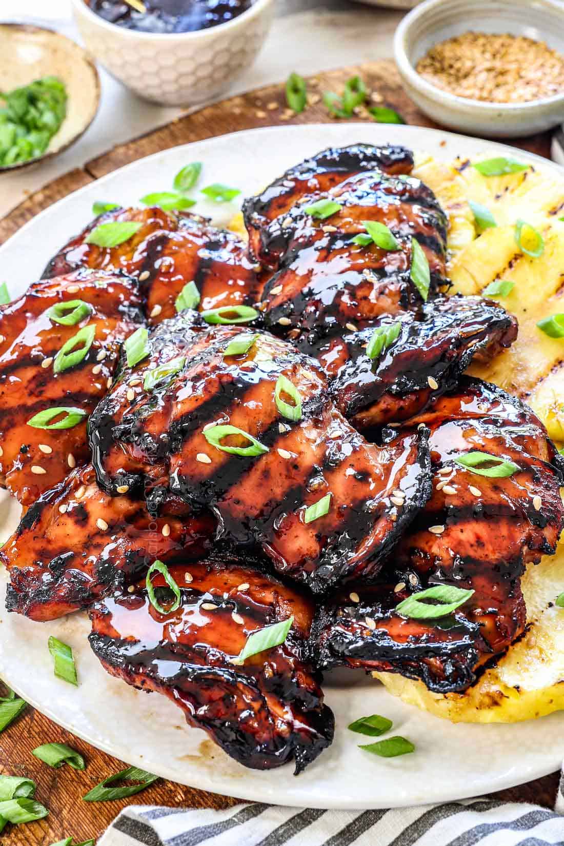 side view of teriyaki chicken recipe being served on a plate with pineapple and extra teriyaki sauce on the side