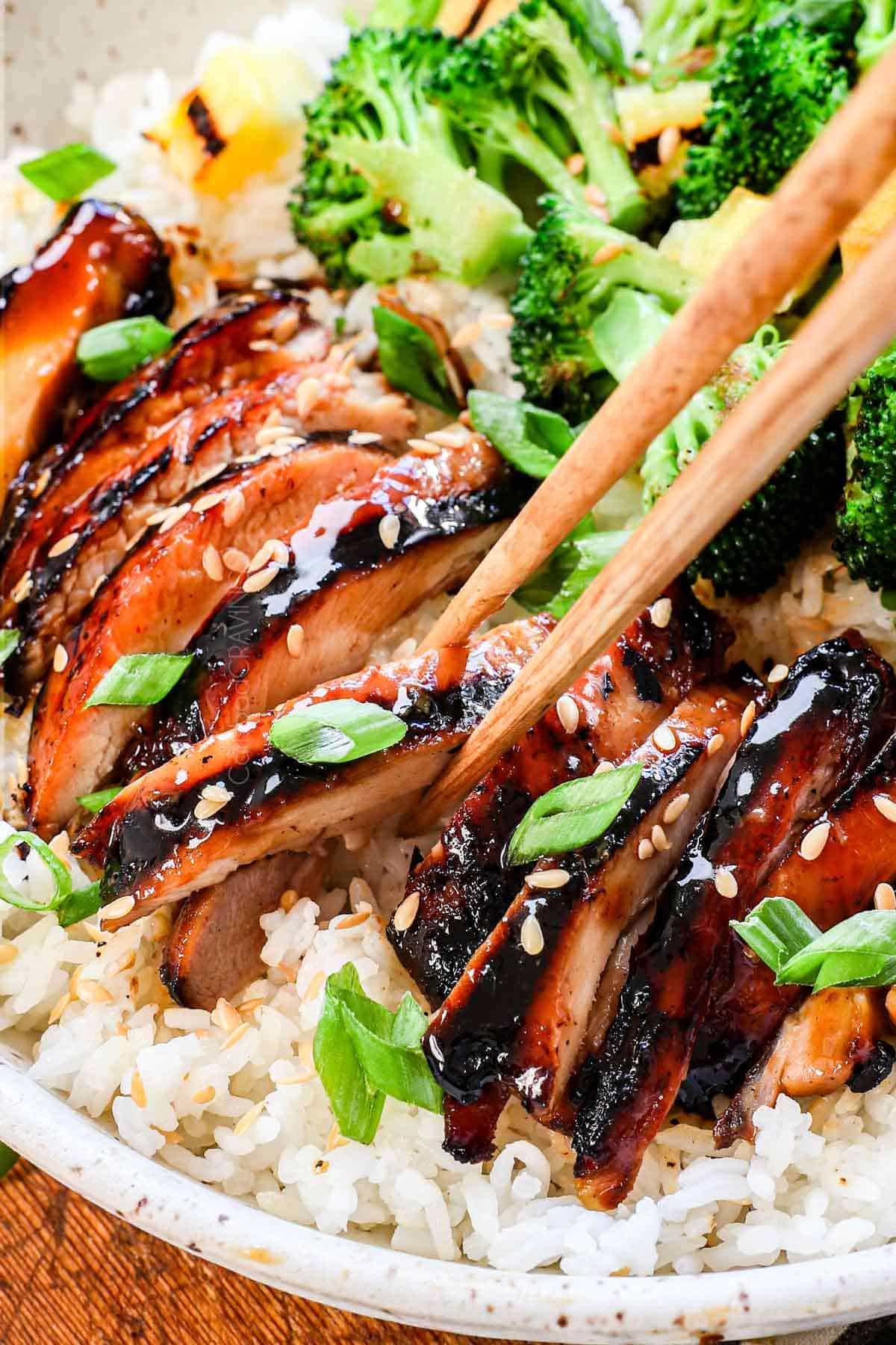 up close of picking up chicken teriyaki with chopsticks showing how juicy it is