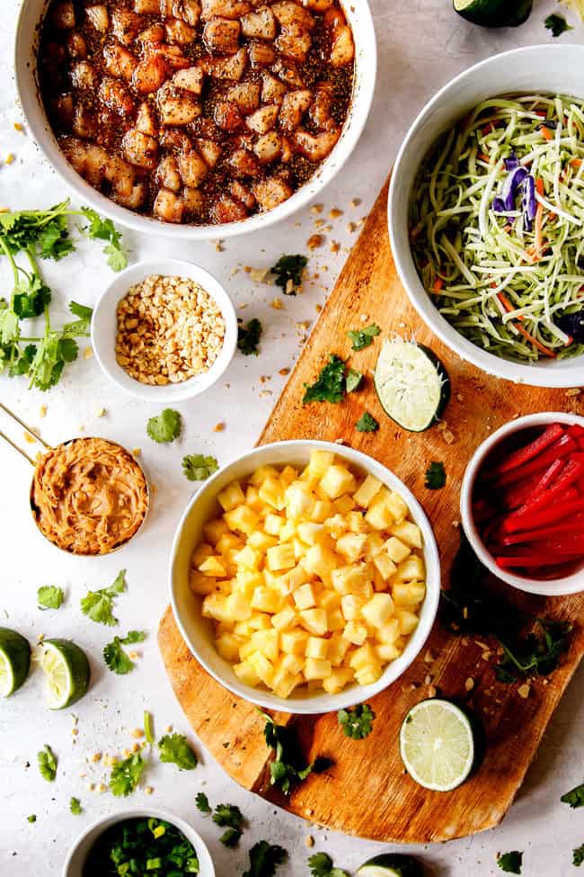 top view of ingredients for Thai chicken tacos - marinating chicken, peanuts, peanut butter, coleslaw, pineapple, bell peppers, limes