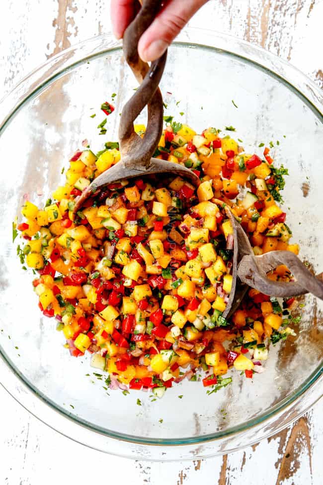 showing how to make mango salsa with two wooden spoons tossing ingredients together