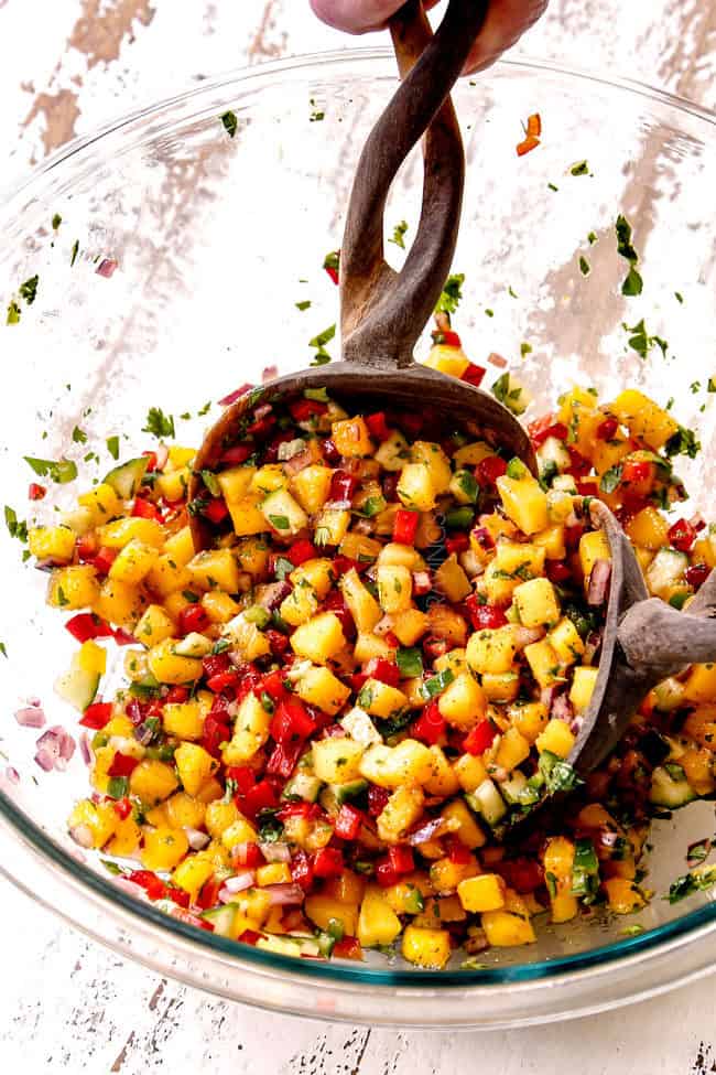 showing how to make mango salsa with two wooden spoons tossing ingredients together