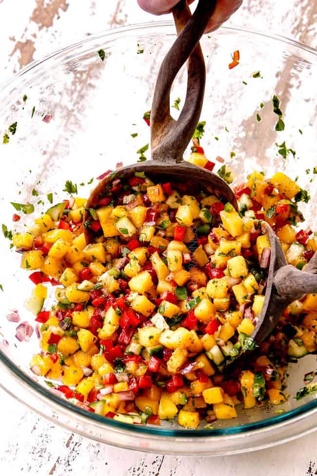 showing how to make mango salsa with two wooden spoons trowinging ingredients together