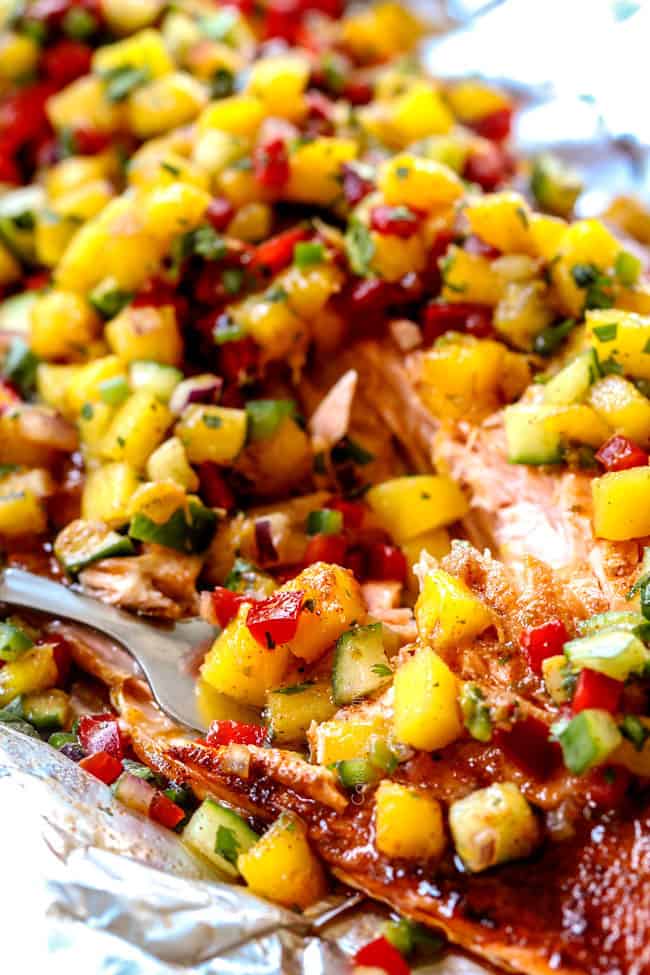 a fork sitting next to oven baked salmon with mango salsa