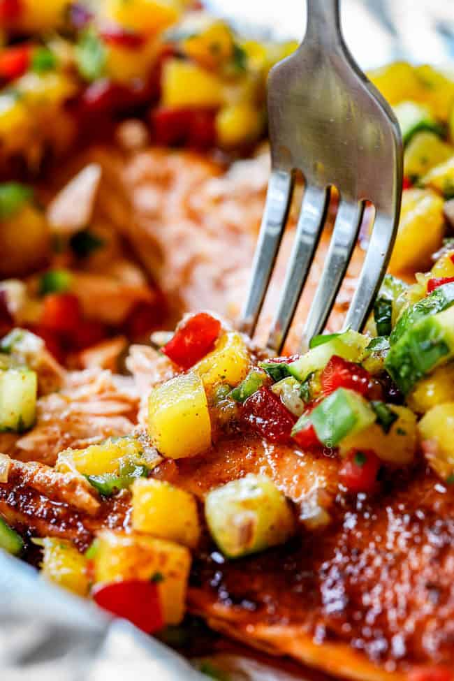 eine Gabel, die in den gebackenen Lachs mit Mango-Salsa beißt