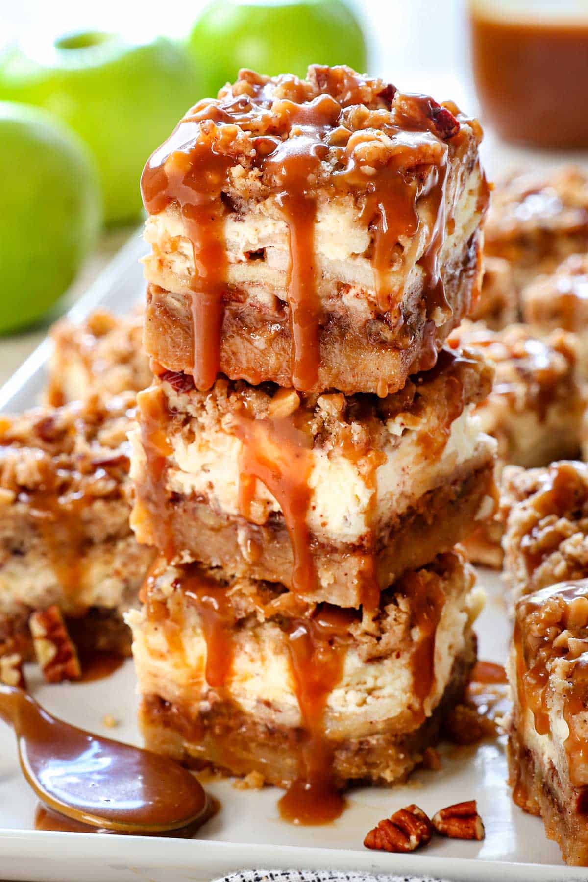 Caramel Apple Cheesecake Bars stacked on a platter drizzled with caramel