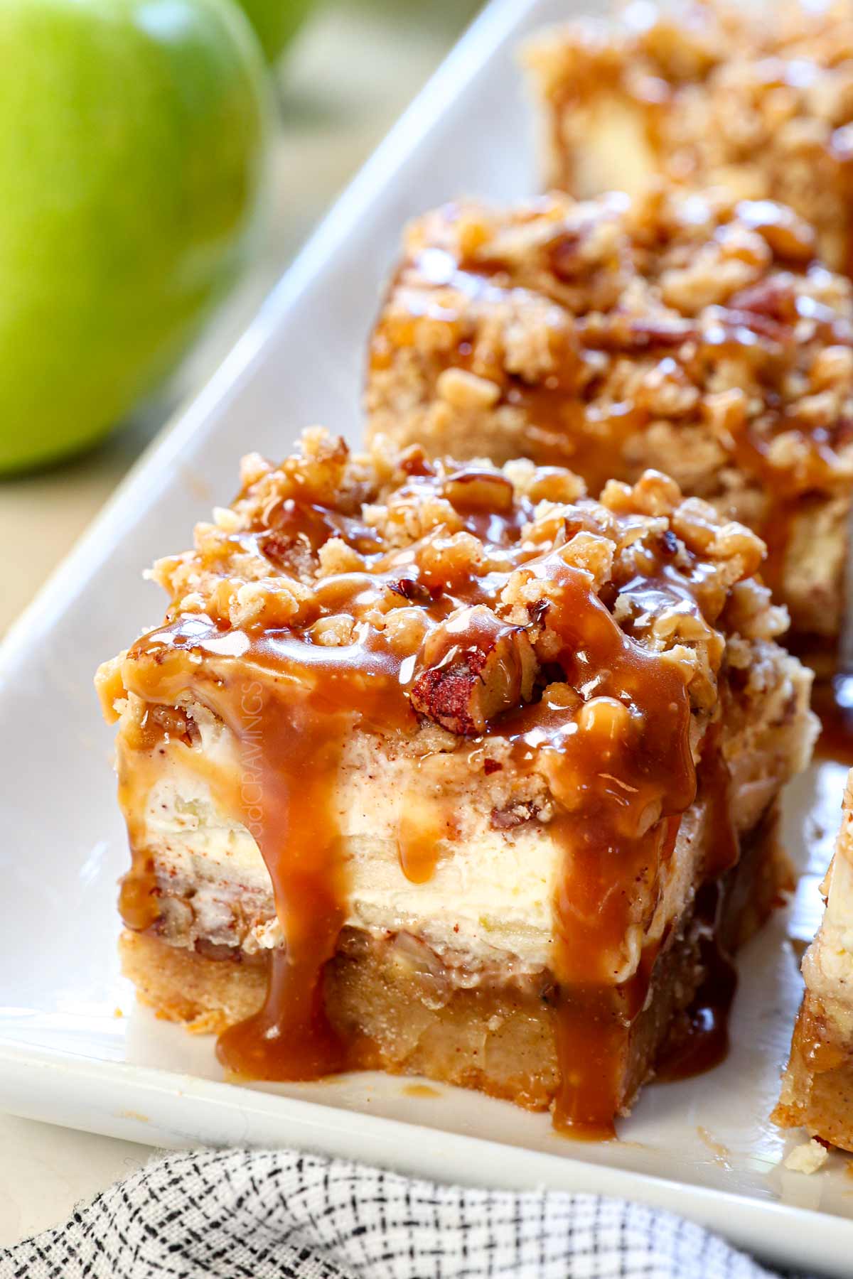 up close of apple cheesecake bars showing the creamy cheesecake and crunchy streusel topping drizzled with caramel